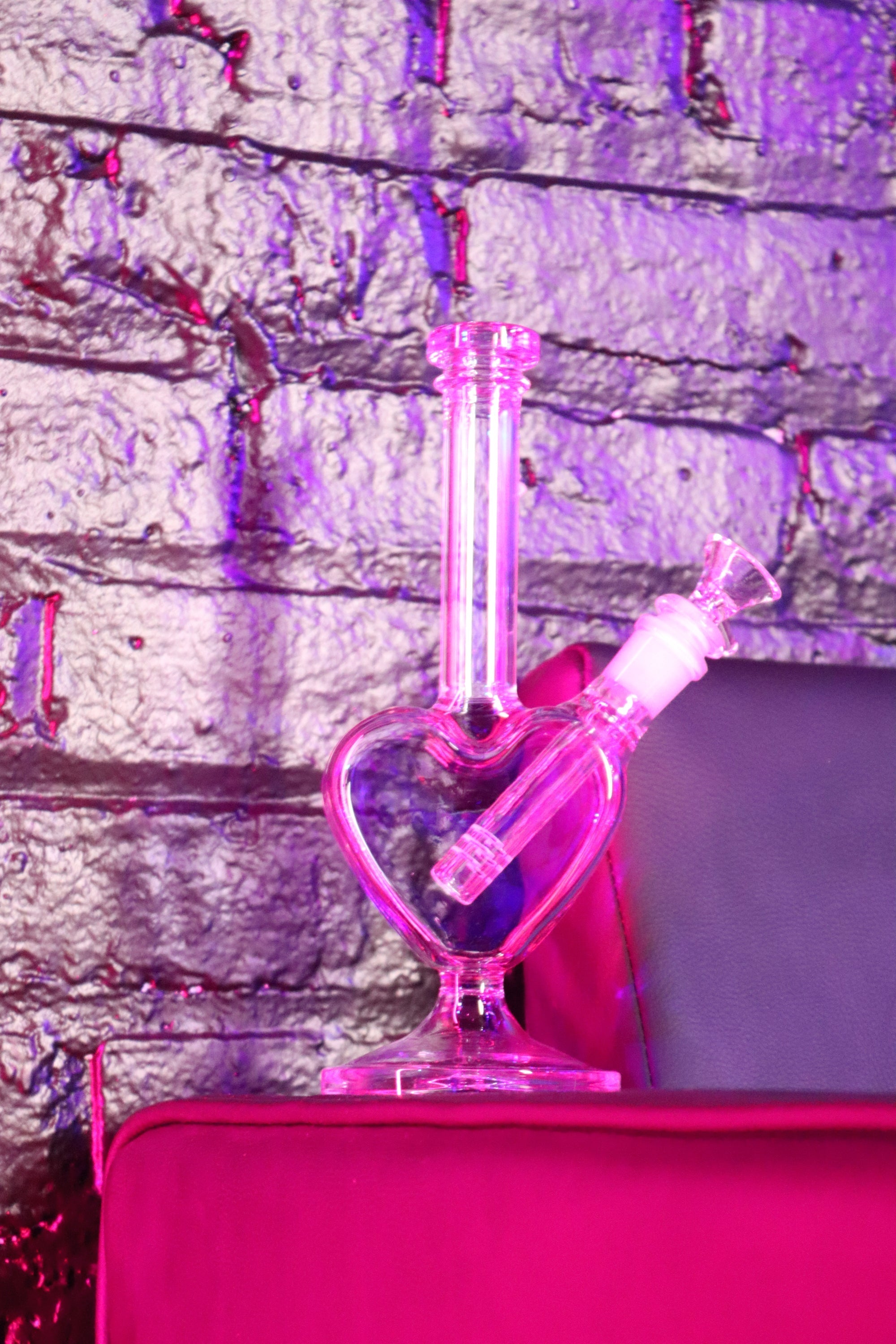 pink bong on a couch against brick wall